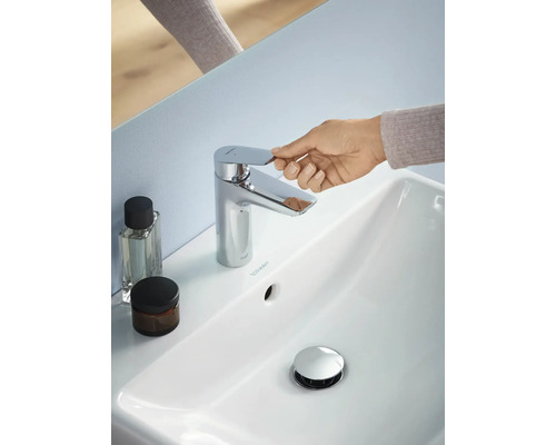 Imaginea unei băi cu o chiuvetă albă, un robinet cromat, o mână care acționează robinetul și două recipiente