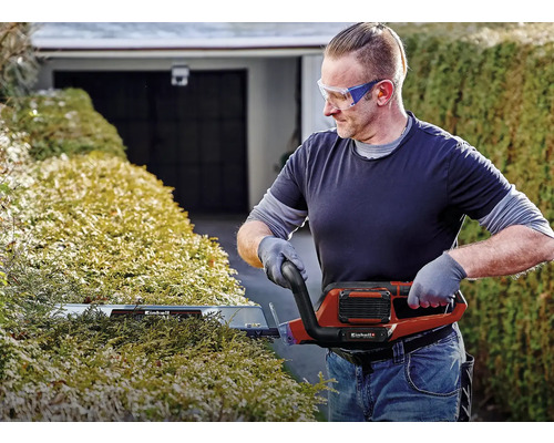 Un bărbat taie un gard viu cu o foarfecă electrică de tuns gard viu de la Einhell.