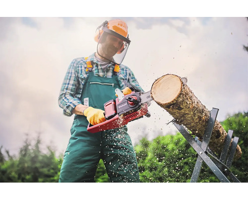 Bărbat cu echipament de protecție taie un trunchi de copac pe un capră cu un ferăstrău cu lanț Einhell