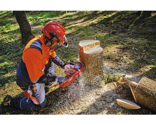 O persoană cu echipament de protecție folosește un motoferăstrău pe un ciot de copac.