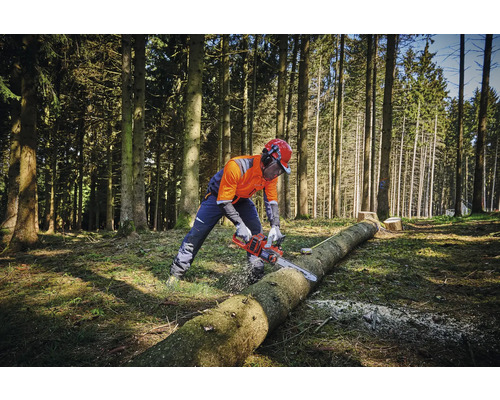 O persoană cu echipament de protecție taie un trunchi de copac în pădure cu un motoferăstrău.