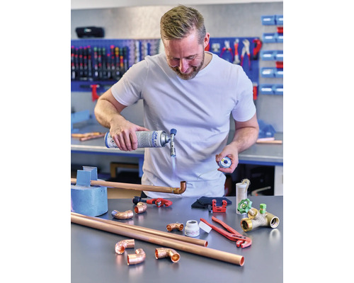 Un bărbat sudează țevi de cupru cu un arzător cu gaz și cositor, înconjurat de fitinguri de țevi de cupru și scule.