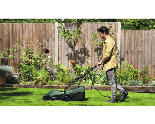 Un bărbat tunde gazonul cu o mașină de tuns iarba electrică într-o grădină.