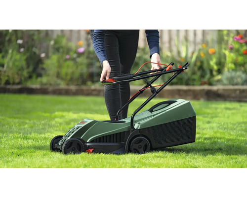 O persoană operează o mașină de tuns iarba verde pe un gazon.