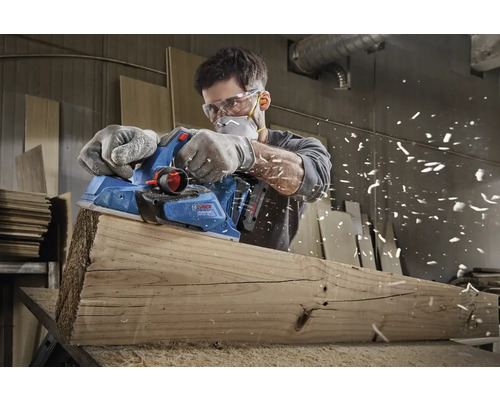 Bărbat rindeluind o scândură de lemn cu o rindelă electrică marca Bosch