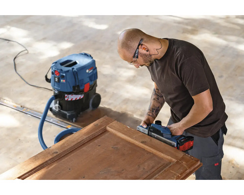 Artizan șlefuind o ușă de lemn cu un rindel electric și un aspirator