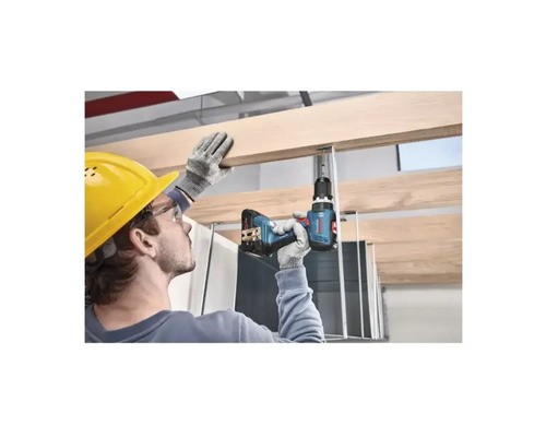 Artizan cu cască de protecție găurește o scândură de lemn pe o structură de tavan cu o bormașină cu acumulator.