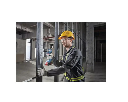 Un bărbat cu cască de protecție și ochelari de protecție folosește o șurubelniță fără fir într-o clădire la roșu.