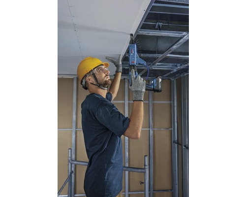 Mester fixând plăci de tavan cu o mașină de înșurubat cu magazie