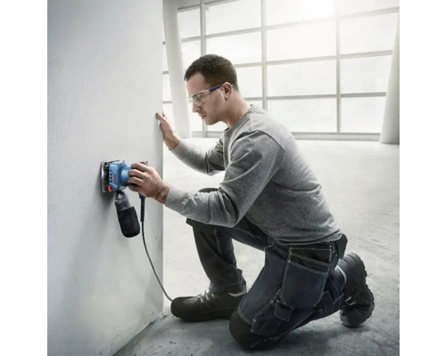 Un bărbat șlefuiește un perete cu o șlefuitoare electrică într-o cameră luminoasă.