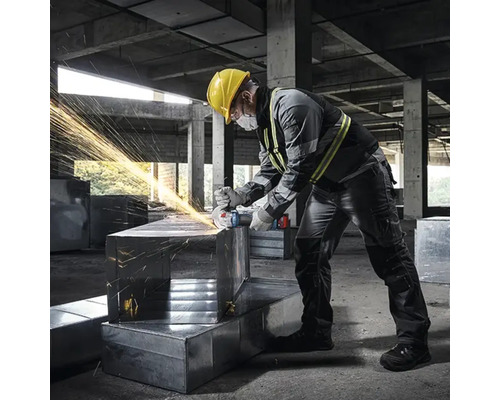 Un bărbat cu cască de protecție șlefuiește metal cu un polizor unghiular, rezultând scântei.