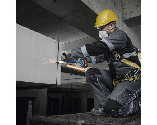 Meșter cu cască de protecție, ochelari de protecție și mască de față lucrând cu un polizor unghiular fără fir.