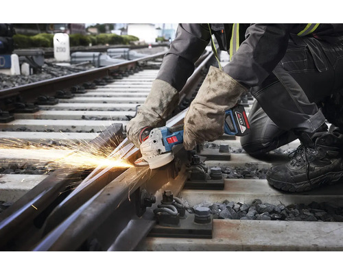 Un muncitor taie o șină de cale ferată cu un polizor unghiular, rezultând scântei.