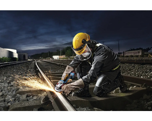 Un muncitor șlefuiește o șină de cale ferată cu un polizor unghiular, creând scântei.