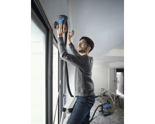 Bărbat pe o scară șlefuind un tavan cu un șlefuitor de tavan, conectat la un aspirator