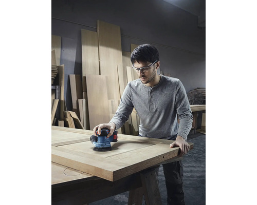 Bărbat șlefuiește o ușă din lemn cu o șlefuitoare excentrică în atelier