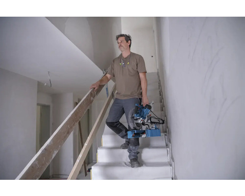 Un meseriaș coboară o scară cu un ferăstrău de panouri într-o casă în construcție.