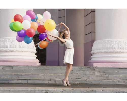 Femeie cu multe baloane în fața unei clădiri