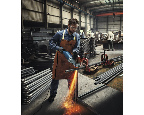 Un bărbat într-un atelier taie o țeavă metalică cu un polizor unghiular, cu scântei zburând.