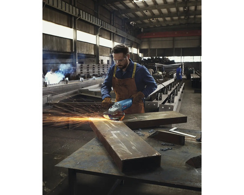 Un bărbat șlefuiește metal cu un polizor unghiular într-un atelier.