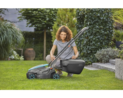 O femeie stă ghemuită în grădină și montează o mașină de tuns iarba cu un coș colector de 30 de litri.