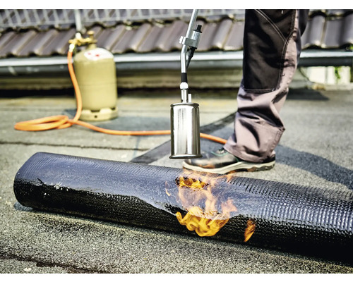 Acoperitorul sudează membrana bituminoasă cu un arzător și o butelie de gaz.