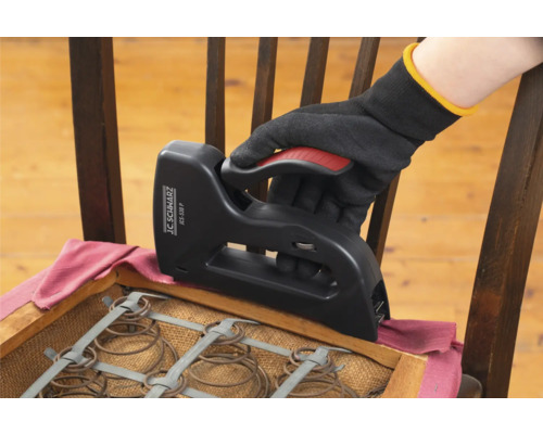 O mână cu mănușă folosește un capsator pentru a retapița un scaun.