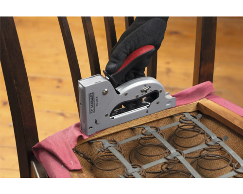O mână cu mănușă fixează o țesătură cu un capsator manual pe un scaun.