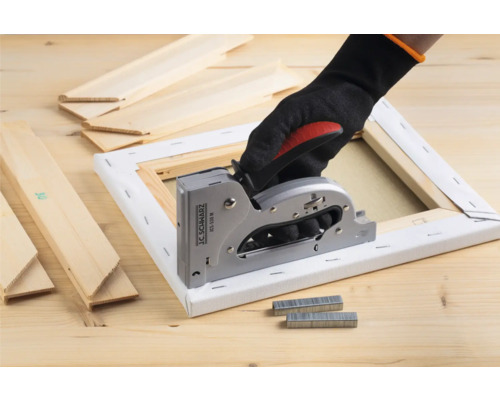 Mână cu mănușă folosind un capsator manual pe o pânză