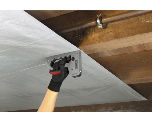 O persoană fixează o folie de protecție împotriva vaporilor cu un capsator de un tavan de lemn.