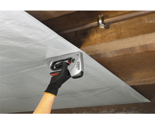 O persoană fixează folie cu un capsator manual de un tavan de lemn.