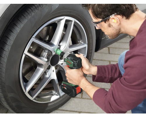 Bărbat schimbând o anvelopă la o mașină cu o cheie de impact fără fir