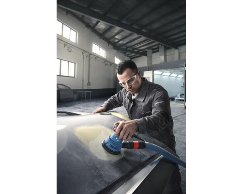 Un bărbat șlefuiește capota unei mașini cu o șlefuitoare excentrică într-un atelier.