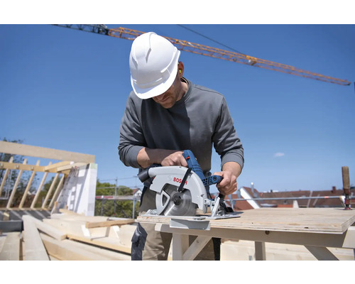 Meșter cu cască de protecție taie lemn cu un circular Bosch pe un șantier.