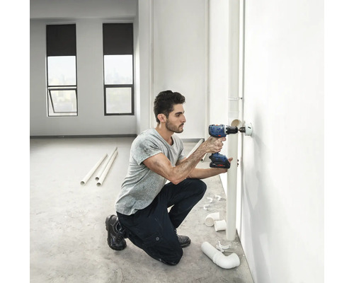 Artizan care gaurește un orificiu cu o șurubelniță fără fir în perete pentru instalarea conductei