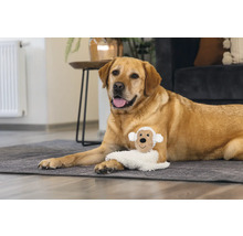 Un labrador stă întins cu o jucărie de pluș în formă de oaie pe un covor.