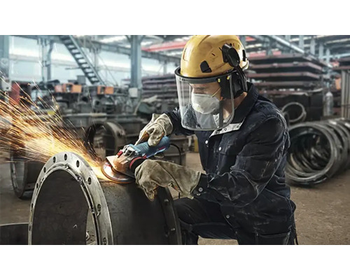 Un muncitor șlefuiește o țeavă metalică cu un flex, rezultând scântei.