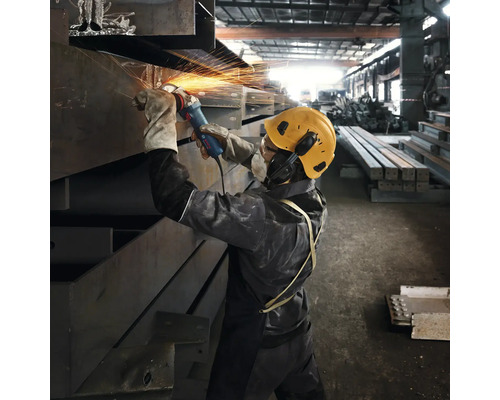 Un muncitor șlefuiește metal cu un polizor unghiular într-o hală de fabrică, în timp ce sar scântei.