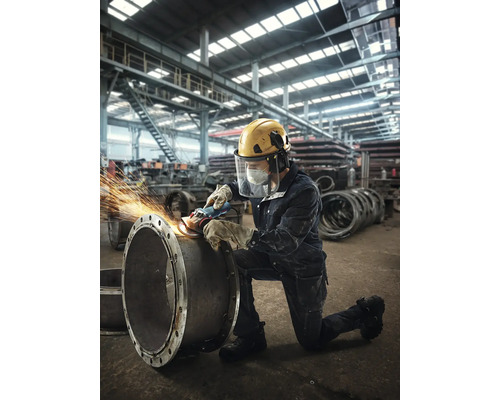 Un muncitor șlefuiește o țeavă cu o mașină de șlefuit într-o hală de fabrică, purtând echipament de protecție.