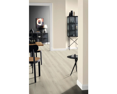 Interior cu podea laminată deschisă la culoare, scaune și obiecte decorative pe mese și într-o vitrină de sticlă.