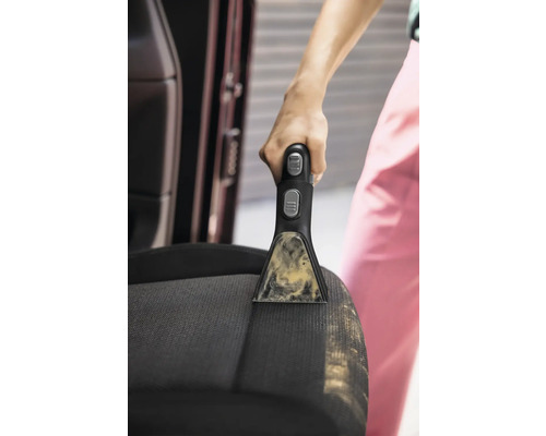 Prim-plan cu o persoană care curăță un scaun de mașină cu un dispozitiv portabil de curățat pete.