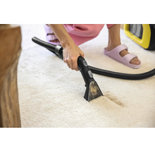 Aspirator de covoare în uz pe un covor de culoare deschisă.