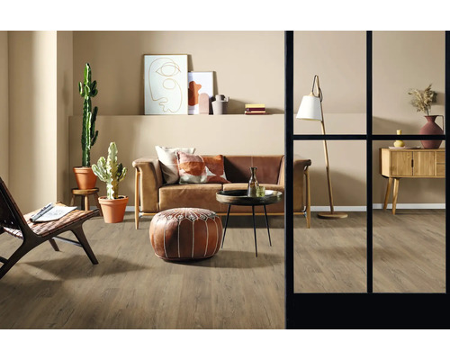 Cameră de zi cu canapea, fotoliu, masă, lampă de podea, comodă, decorațiuni și plante de interior pe podea de lemn.