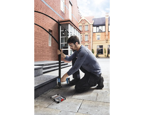 Un bărbat fixează o balustradă de scările unei clădiri cu o șurubelniță fără fir.