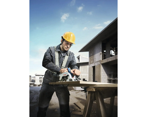 Un muncitor în construcții taie o scândură de lemn cu un fierăstrău circular manual Bosch pe un șantier.