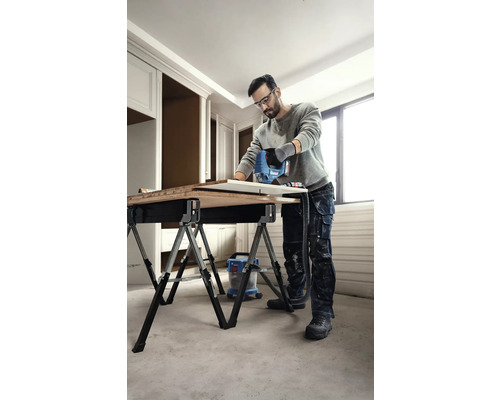 Un bărbat taie o piesă de prelucrat pe un banc de lucru cu un ferăstrău vertical, folosind un aspirator.