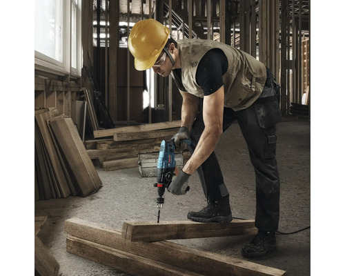 Un muncitor în construcții găurește cu o mașină de găurit cu percuție o scândură de lemn.