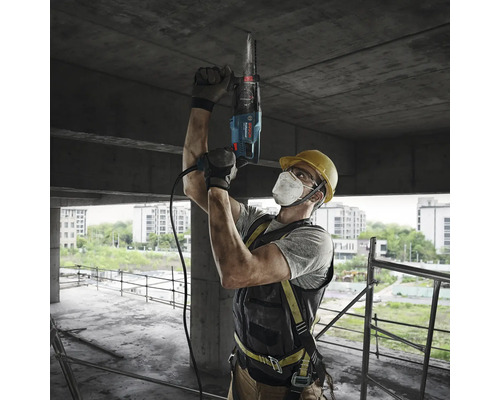 Un muncitor în construcții forează cu un ciocan rotopercutor într-un tavan de beton pe un șantier.