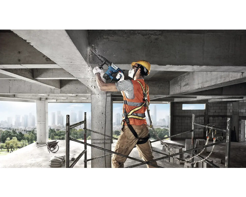 Muncitor în construcții cu ciocan demolator care efectuează lucrări de betonare pe un șantier.