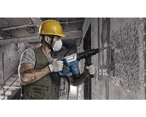 Un meșter găurește un perete de beton cu un ciocan rotopercutor.